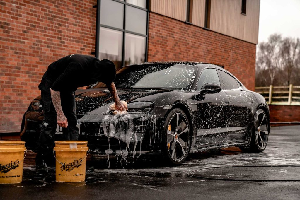 Person hand-washing a black car outside